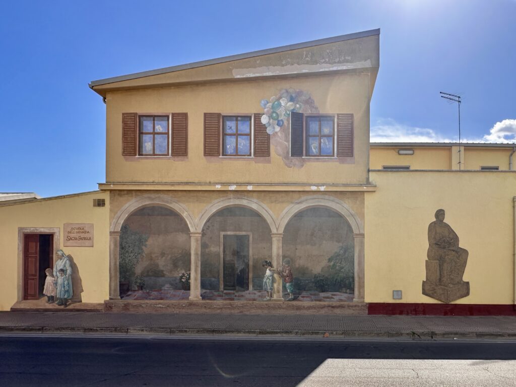 Murale Il Loggiato dell'Asilo delle Suore di Angelo Pilloni in via Cagliari a San Sperate: loggiato dipinto a tre archi con due bambini che giocano, una suora con due bambini sulla porta e palloncini che escono da una finestra