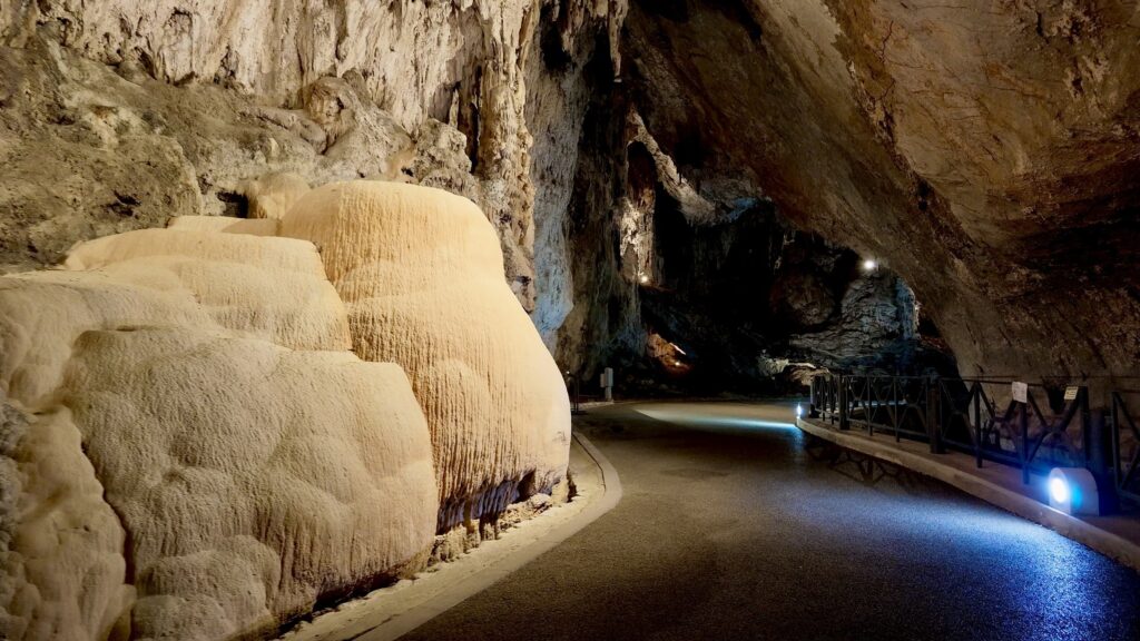 Grande colata di calcare color crema accanto alla strada illuminata che attraversa la Grotta di San Giovanni