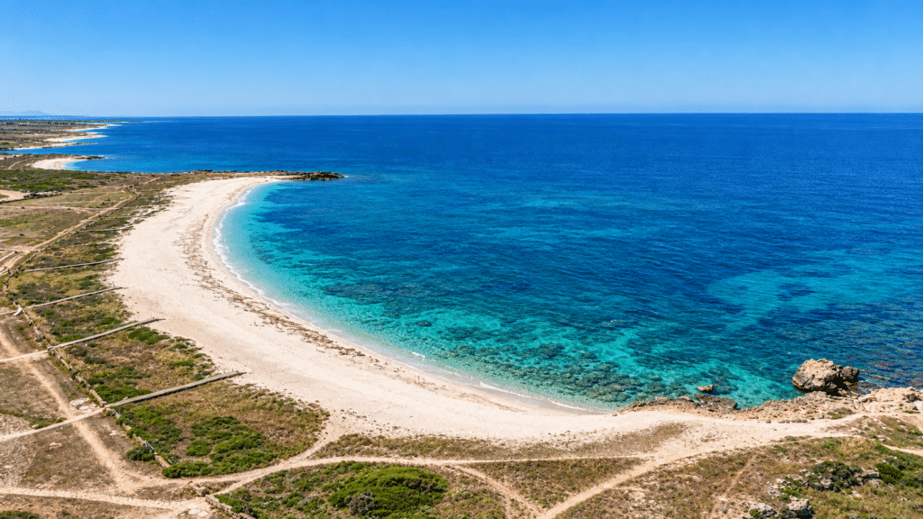 Vista aerea della spiaggia di Is Arutas, con la riva chiara a mezzaluna, il mare turchese e le passerelle in legno tra la macchia