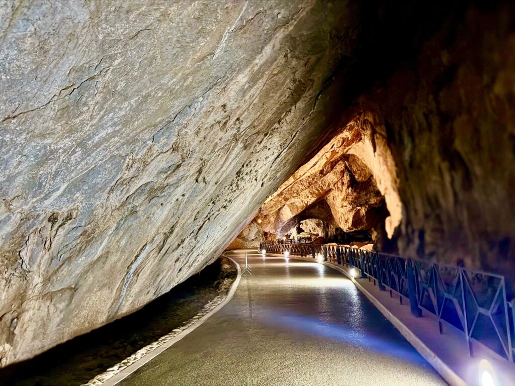 Enorme parete di roccia inclinata sopra la strada, con il letto asciutto del torrente sul lato sinistro