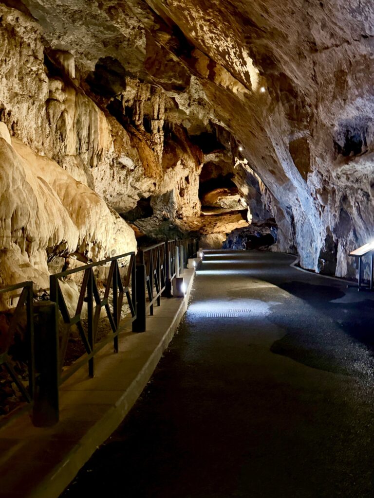 Strada pedonale con ringhiera che corre tra pareti di calcare e concrezioni illuminate