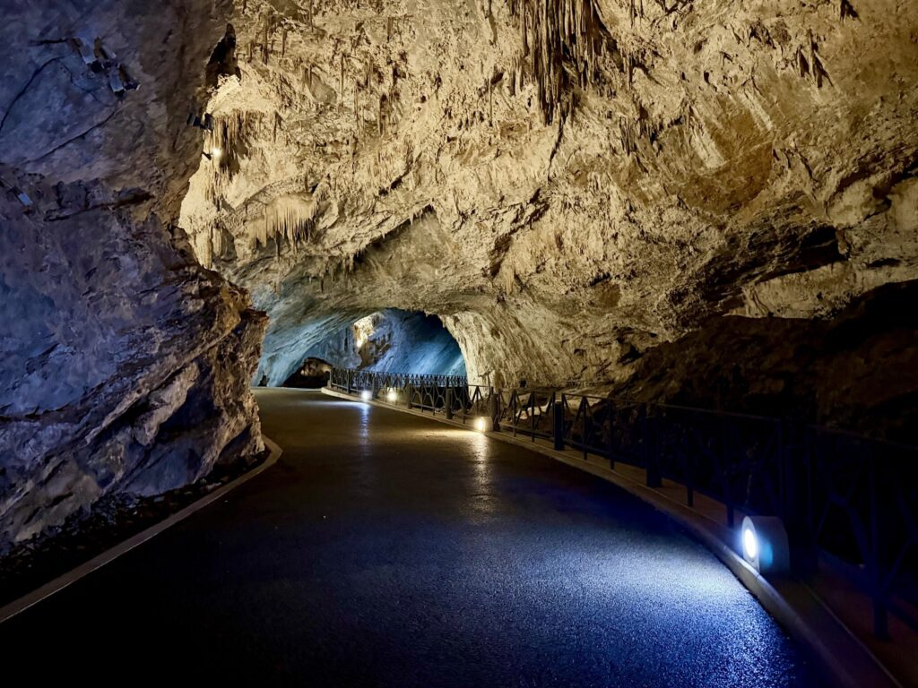 Volta della galleria principale con stalattiti sottili sopra la strada in curva e le luci a terra